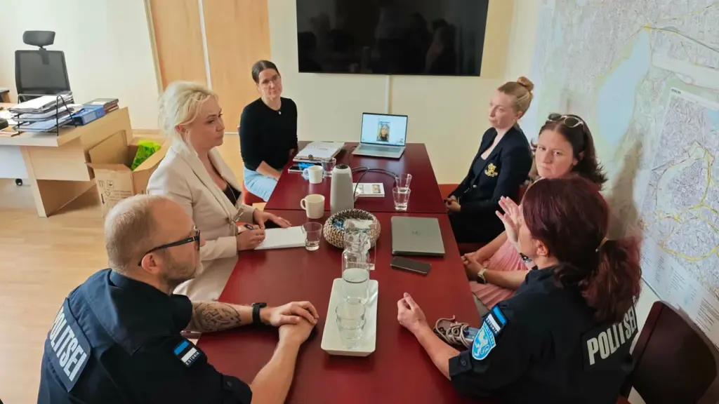 Politseinikud ja ametnikud istuvad koosolekulaua ümber, vesteldes kontoriruumis, kus seinal on suur linnakaart.