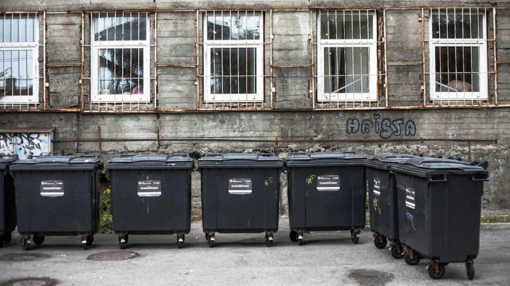 Rida prügikonteinereid Tallinnas asuva vana hoone ees halli taeva all.